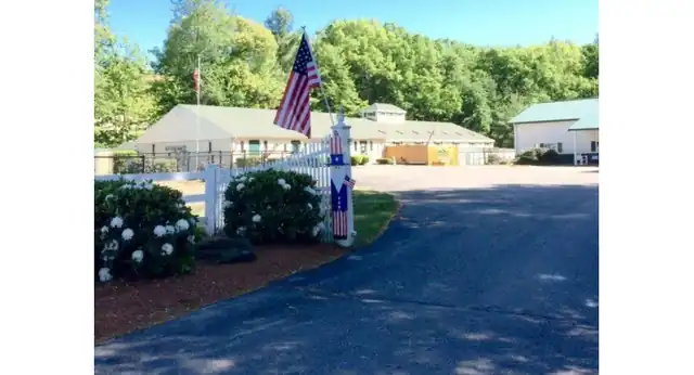 The Clinton Road entrance: a paved drive, white fence, flag and the two kennel buildings under the trees